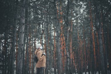 Tıbbi maskeli genç sarışın bir kadın kış ormanında yürüyor..