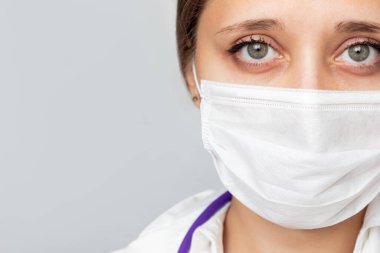 Gri bir arka planda izole edilmiş tıbbi maskeli bir kadın doktorun yüzünü yakından çek. Metin veya tasarım için boş kopyalama alanı