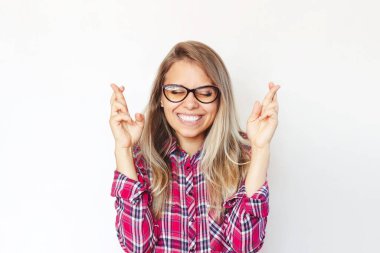 Kırmızı ekose gömlekli ve gözlüklü gülümseyen genç bir sarışın kız şans dilemek için şans diliyor ya da beyaz arka planda izole edilmiş sınavları bekliyor.