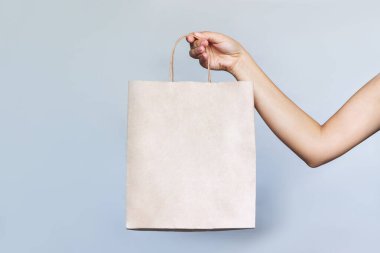 Açık gri bir arkaplanda izole edilmiş bir kadın elinde logo için boş alan olan kâğıt çevre dostu çanta. Model, metin ya da tasarım için şablon. Alışveriş ve moda.