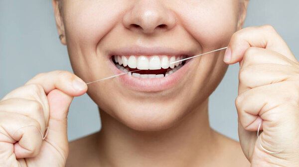 Cropped shot of a young beautiful caucasian woman flossing her teeth isolated on a gray background. Oral hygiene, dental health care, morning and evening routine. 