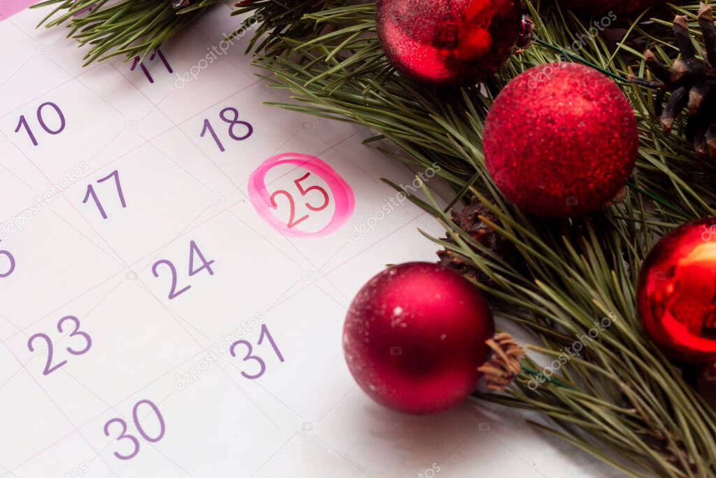 Open calendar of 2021 with a mark on the date of December 25. A branch of Christmas tree with toy balls and cones. Atmosphere of the holiday. Christmas content. Selective focus