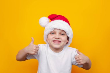 Sarı arka planda izole edilmiş Noel Baba şapkası takan küçük şirin çocuk.