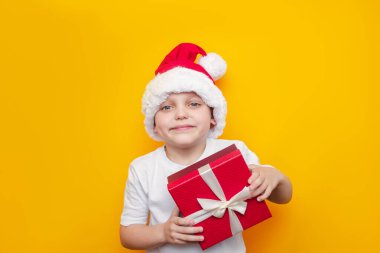 Sarı arka planda hediye kutusu olan küçük sevimli bir çocuk.