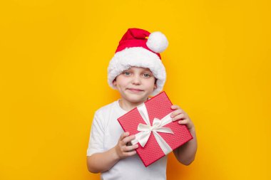 Sarı arka planda hediye kutusu olan Noel Baba şapkalı şirin çocuk.