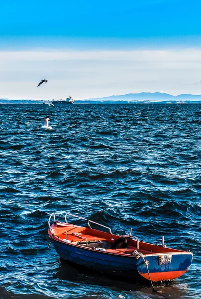 Leeres Fischerboot im welligen Meer mit Bergen und Leuchtturm Stockbild