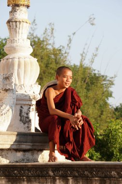 Manastırda oturan gülümseyen Asyalı genç keşişin samimi portresi.