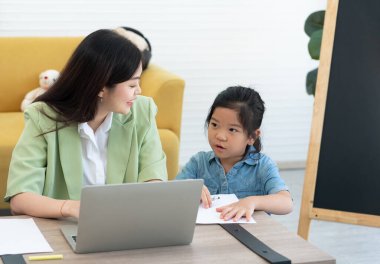 Genç Asyalı anne çocuğuna oturma odasında ödev yapmayı öğretiyor. Evde eğitim kavramı