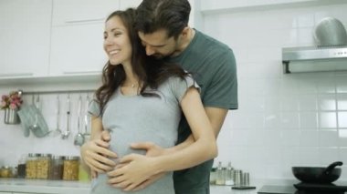 caucasian man hugging his pregnant wife in kitchen