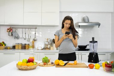 Hamile kadın kulaklık takıyor ve mutfakta akıllı telefon kullanıyor.