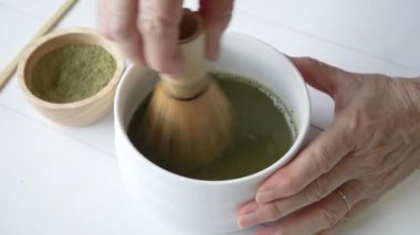 Matcha Green Tea 'yi seremonide karıştırmak için Bambu çırpıcı kullanan Kadının Eli' ni kapat