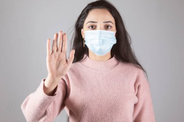Genç kadın tıbbi maske ve dur işareti ile karşı karşıya.