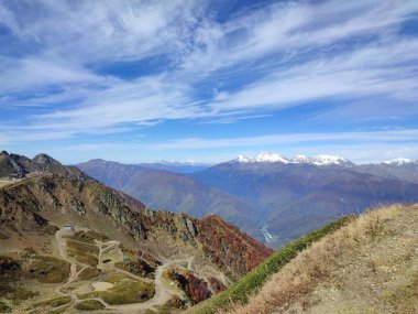 A road in the mountains leading to snow-capped peaks under a blue sky on a sunny autumn day