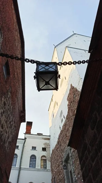 An old street lamp hanging on a chain in the courtyard of a medieval castle in Vyborg against the background of a high tower