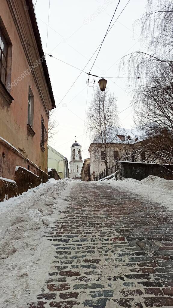 Cobblestone winter street of the ancient city of Vyborg in snowdrifts on a cloudy day illuminated by a lantern