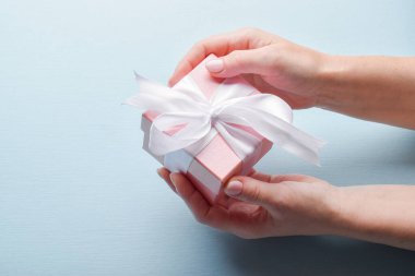 Üstten bakınca bir kadının elinde mavi arka planda beyaz kurdeleli pembe bir hediye kutusu var. Mutlu yıllar, mutlu Anneler Günü, düğün, yıldönümü, Sevgililer Günü kartı.