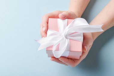 Üstten bakınca bir kadının elinde mavi arka planda beyaz kurdeleli pembe bir hediye kutusu var. Mutlu yıllar, mutlu Anneler Günü, düğün, yıldönümü, Sevgililer Günü kartı.