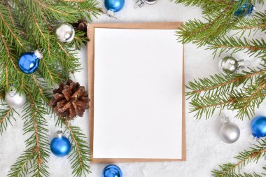 Bir tane boş kartpostal, karda, üzerinde Noel ağacı ve mavi cam toplar olan bir zarf üzerinde duruyor. Pankart, davetiye, kartpostal. Düz, düz, düz, Üst Manzara, Üst Manzara