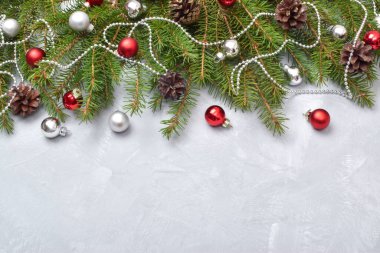 Kırmızı cam toplarla Noel kompozisyonu. Noel ağacının dalları gri bir arka planda süslenmiştir..