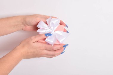 Mavi manikürlü, elinde beyaz kurdeleli pembe bir hediye kutusu olan bir kadının üst görüntüsü. Sevgililer günü kartı. Kopyalamak için yer var. Düz konum, üst görünüm.