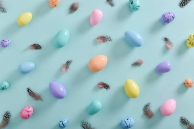 Pastel tonlarda renkli yumurtalar ve açık mavi arkaplanda tüyler. Paskalya 'nın minimum kompozisyonu. Yumurtalı bir tatil kartı. Boşluğu kopyala