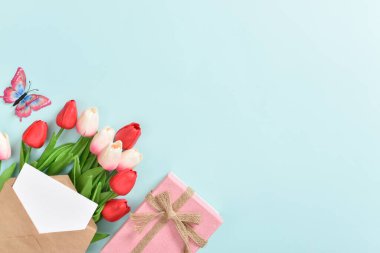 Üzerinde kartpostal olan bir buket lale ve açık mavi arka planda bir hediye. Uluslararası Kadınlar Günü, 8 Mart, Anneler Günü, Paskalya, doğum günü. Kopyalamak için yer var. Düz konum, üst görünüm.