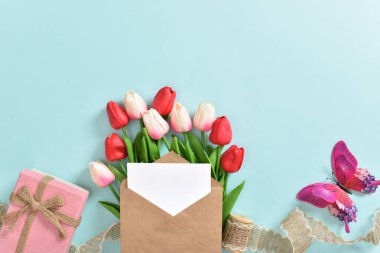 Üzerinde kartpostal olan bir buket lale ve açık mavi arka planda bir hediye. Uluslararası Kadınlar Günü, 8 Mart, Anneler Günü, Paskalya, doğum günü. Kopyalamak için yer var. Düz konum, üst görünüm.