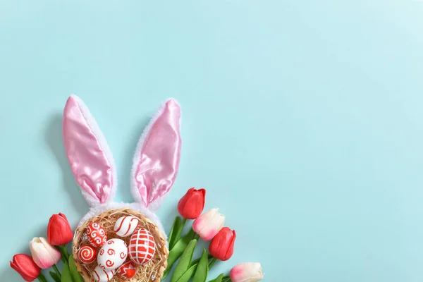 Фон с кроличьими ушами, тюльпанами и пасхальными яйцами на синем фоне. — стоковое фото
