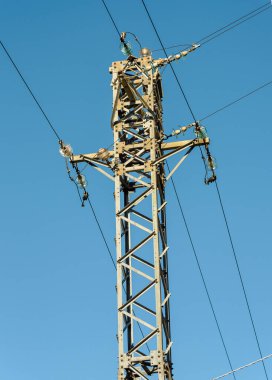 Mavi gökyüzüne karşı yüksek voltajlı elektrik direği.