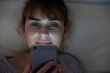 Woman at night admiring her lit smartphone. Addictive behavior.