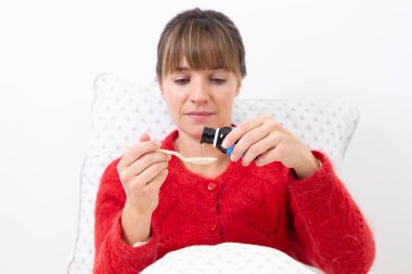 Young woman in bed suffering from a cold with syrup.