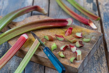 Close-up of rhubarb cut into small pieces with a knife on a cutting board.