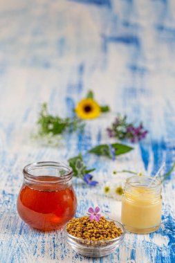 Honey, pollen and royal jelly with medicinal flowers in the background deposited on an old board.