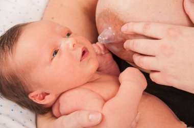 Mother breast feeding baby with silicon nipple protection.