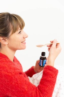 A young woman in bed suffering from a cold with cough syrup.