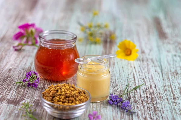 Honey, pollen and royal jelly surrounded by medicinal flowers deposited on an old board.