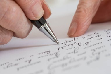 Senior woman writing on a white sheet.