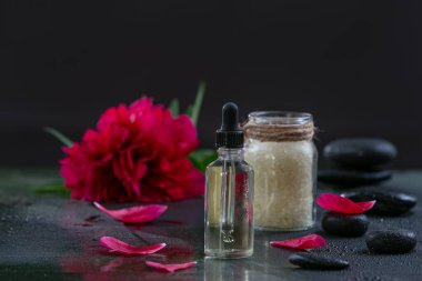 SPA peony, salt, hot stones and essential oil of peony on black background.