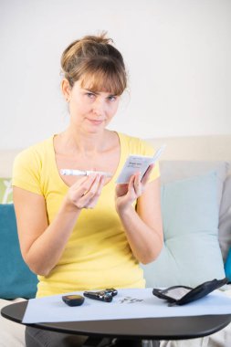 Diabetic woman reading the instructions for use of a kit to measure her sugar level and then inject herself with insulin.