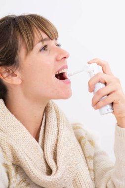 A woman with a sore throat using a mouth spray. clipart