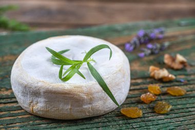 Close-up of saint-nectaire (cheese) alone on an old wooden board with a sprig of tarragon.