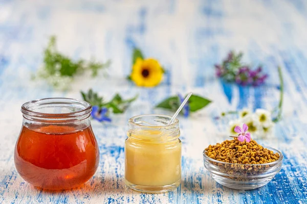 Honey, pollen and royal jelly with medicinal flowers in the background deposited on an old board.
