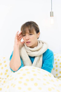 A young woman wrapped up in bed suffering from a flu-like condition with a migraine.