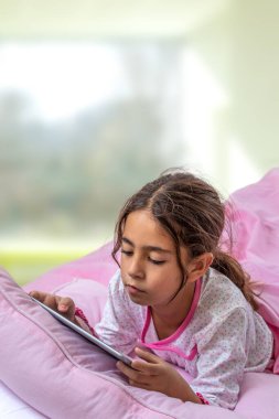 Küçük kız dijital tablet kullanıyor ve yatakta oynuyor..