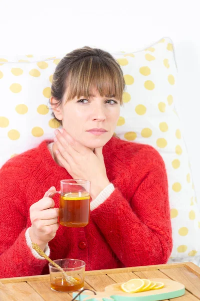 Young woman in bed with a slice of lemon, herbal tea and honey.