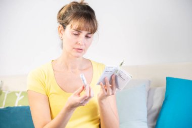 Diabetic woman reading the instructions for use of a kit to measure her sugar level and then inject herself with insulin.