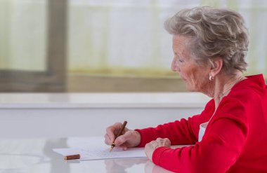 Senior woman writing on a white sheet.