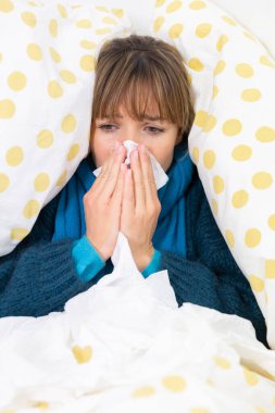 Young woman in bed suffering from a cold with handkerchiefs.