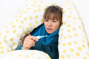 A young woman in bed suffering from a flu-like condition with a thermometre.