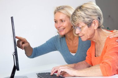 A woman in her fifties helping an elderly woman to use a computer.